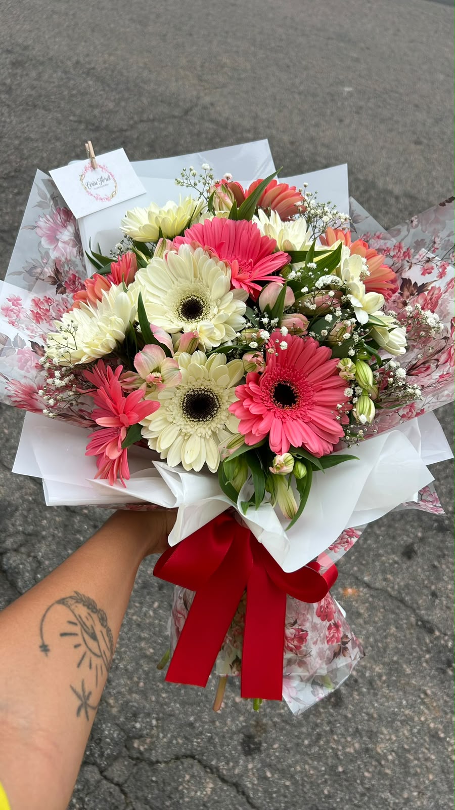Buquê de gérberas rosas e brancas com alstroemérias e mosquitinho, em papel floral e laço vermelho