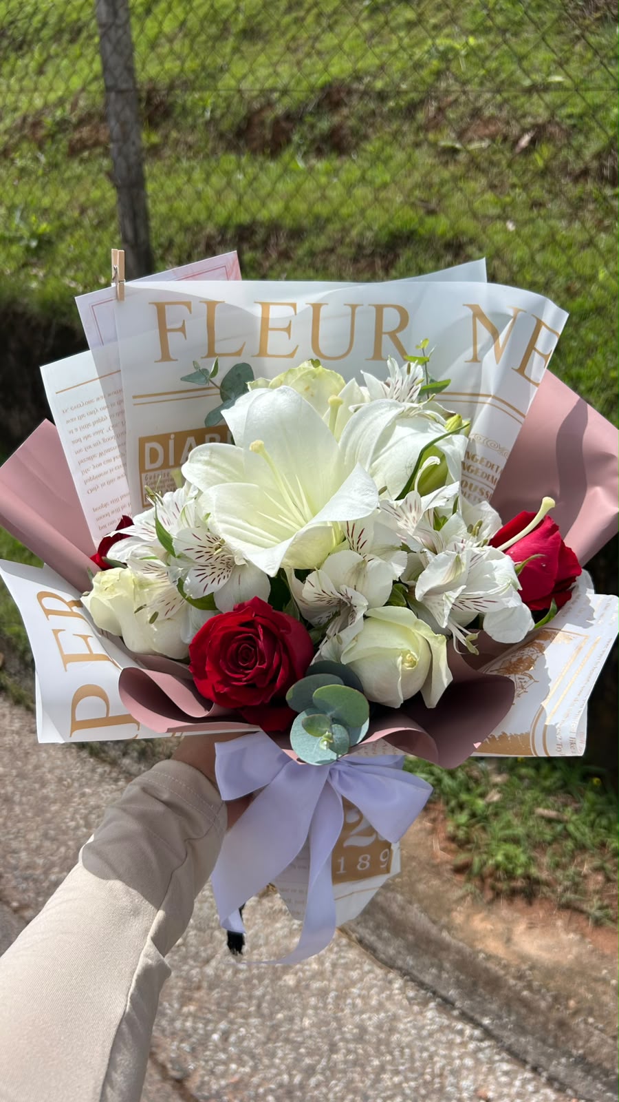 Buquê de lírio branco, alstroemérias, rosas brancas e vermelhas em papel estilo jornal e rosé