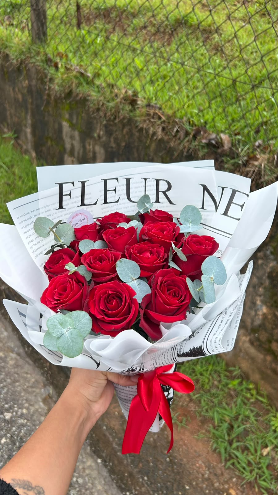 Buquê de rosas vermelhas com eucalipto em papel estilo jornal e laço vermelho
